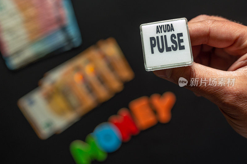 一名男子的两根手指拿着赌场机器的按钮，上面写着“ayuda, pulse”(按，帮助)。下面是一堆模糊的欧元纸币，可以辨认出“钱”这个词。